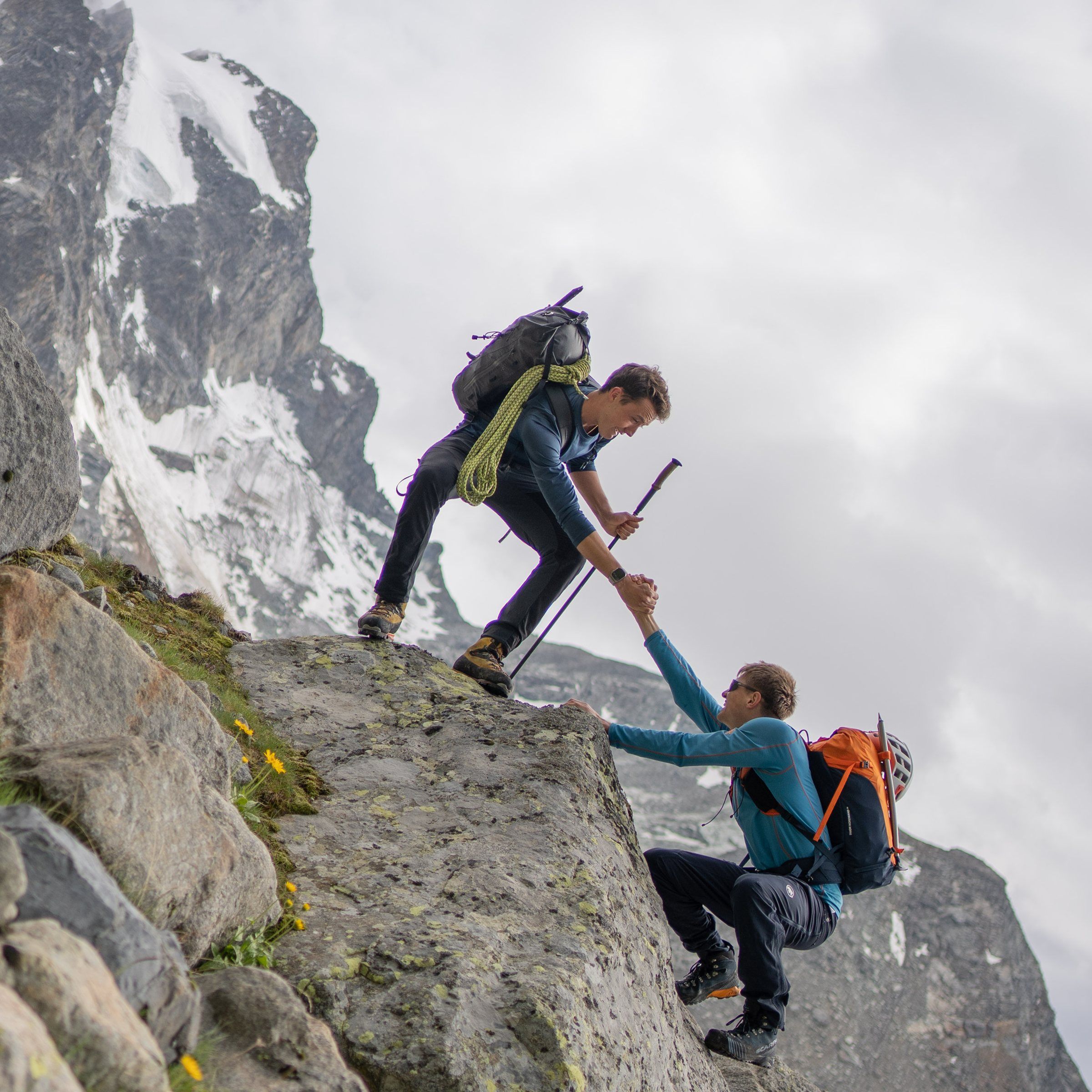 Ein Bergsteiger hilft einem anderen mit der Hand über eine Felsstufe