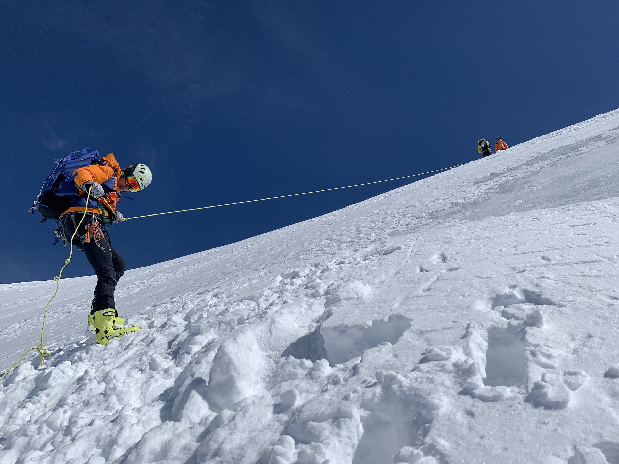 Seilschaft mit Ski steigt einen steilen Firnhang unter blauem Himmel hinauf